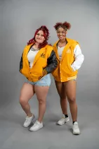 Classic Varsity Jacket 49 Two women wearing Reign Gear yellow and white water-repellent hooded varsity jackets.